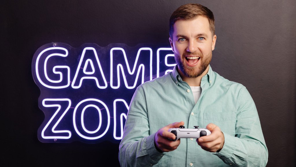 Man holding a game controller in front of game zone neon sign