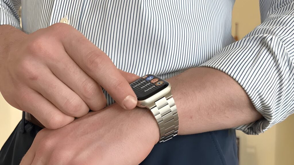 Person wearing a blue-and-white striped dress shirt uses an Apple Watch with a silver metal link band on their wrist