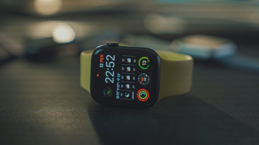 Apple Watch with a light-colored sport band resting on a desk, displaying a detailed watch face