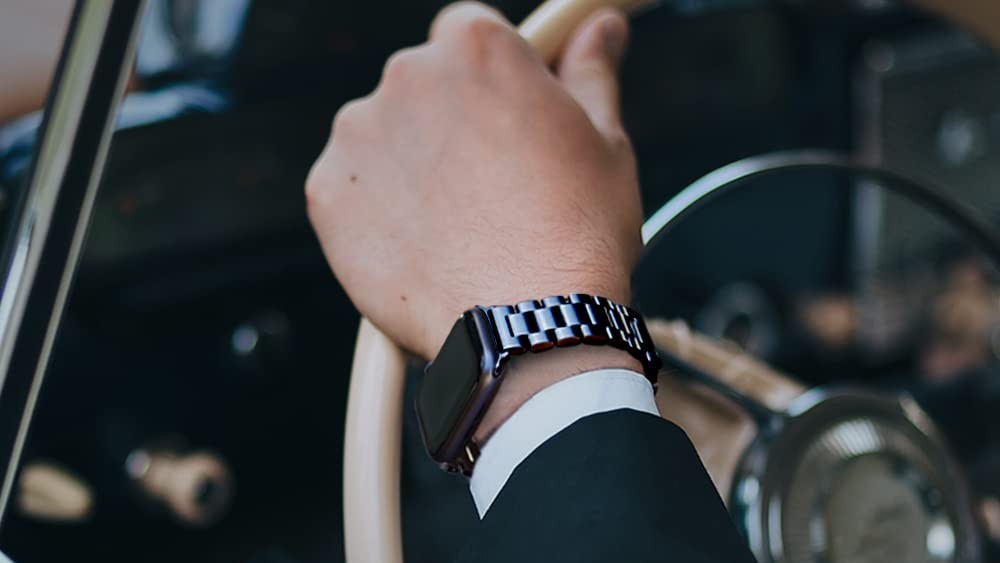 Person wearing an Apple Watch with a black metal link band while holding a steering wheel
