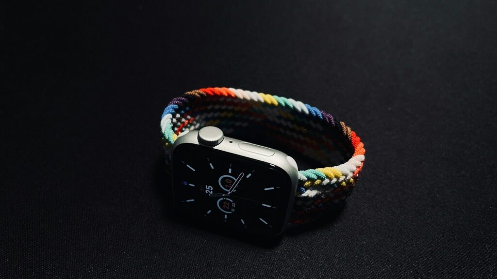 Apple Watch with a colorful braided band resting on a dark surface under dramatic lighting