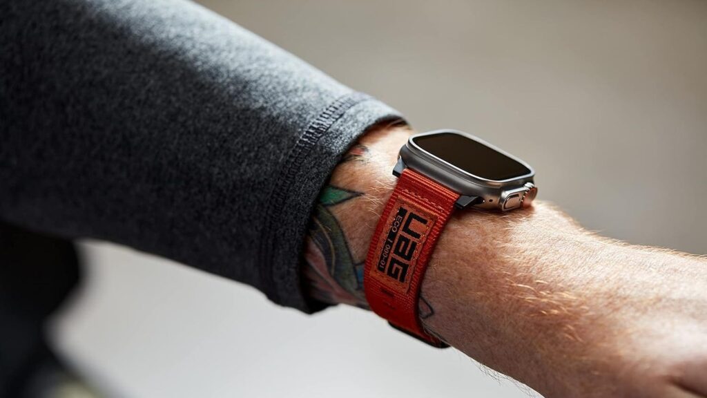 Apple Watch Ultra worn with an orange woven fabric band on a tattooed wrist