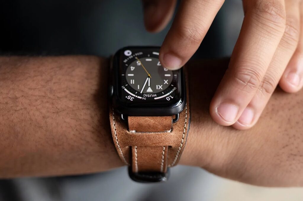 Person interacting with an Apple Watch fitted with a brown leather cuff-style band