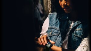 Person using an Apple Watch with a light-colored sport band while wearing a denim vest