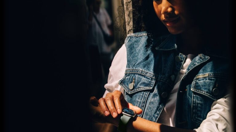 Person using an Apple Watch with a light-colored sport band while wearing a denim vest