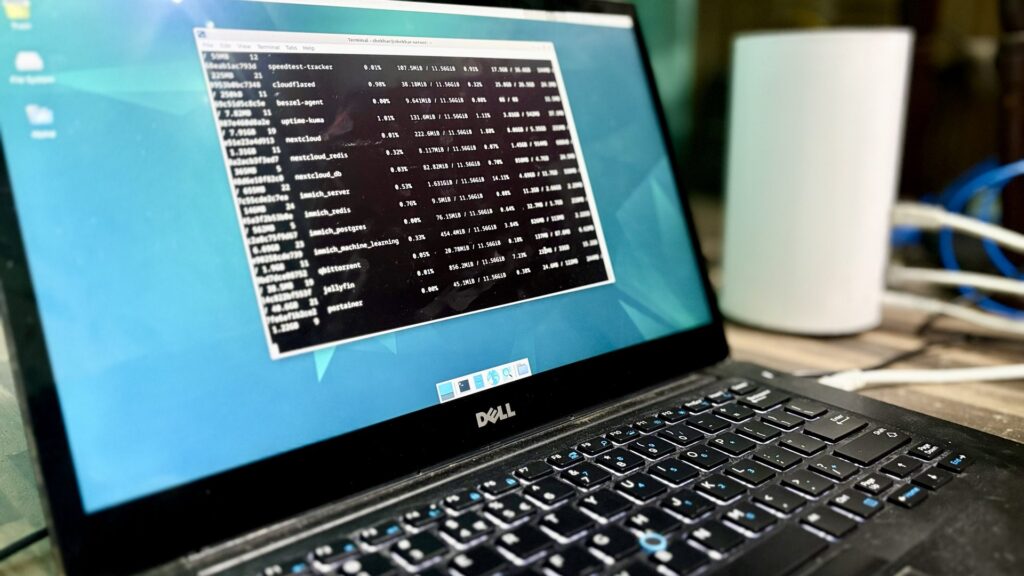 A Dell laptop displays a terminal window with a data table showing process names and performance metrics in monospace font.