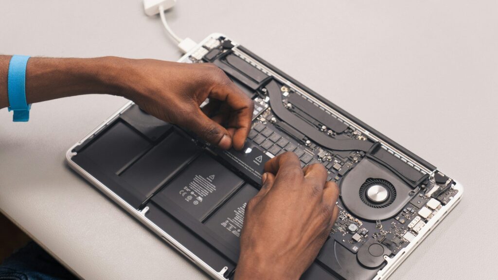Technician's hands removing internal components from an open laptop displaying circuit board and battery.