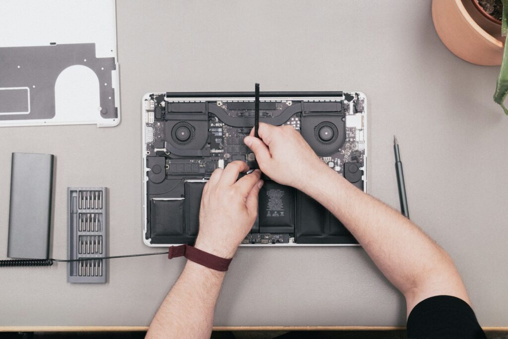 Technician's hands disassembling a laptop's internal components on a work surface.