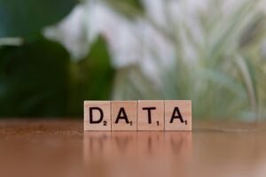 Wooden Scrabble tiles spelling DATA on a reflective surface with blurred green foliage behind.