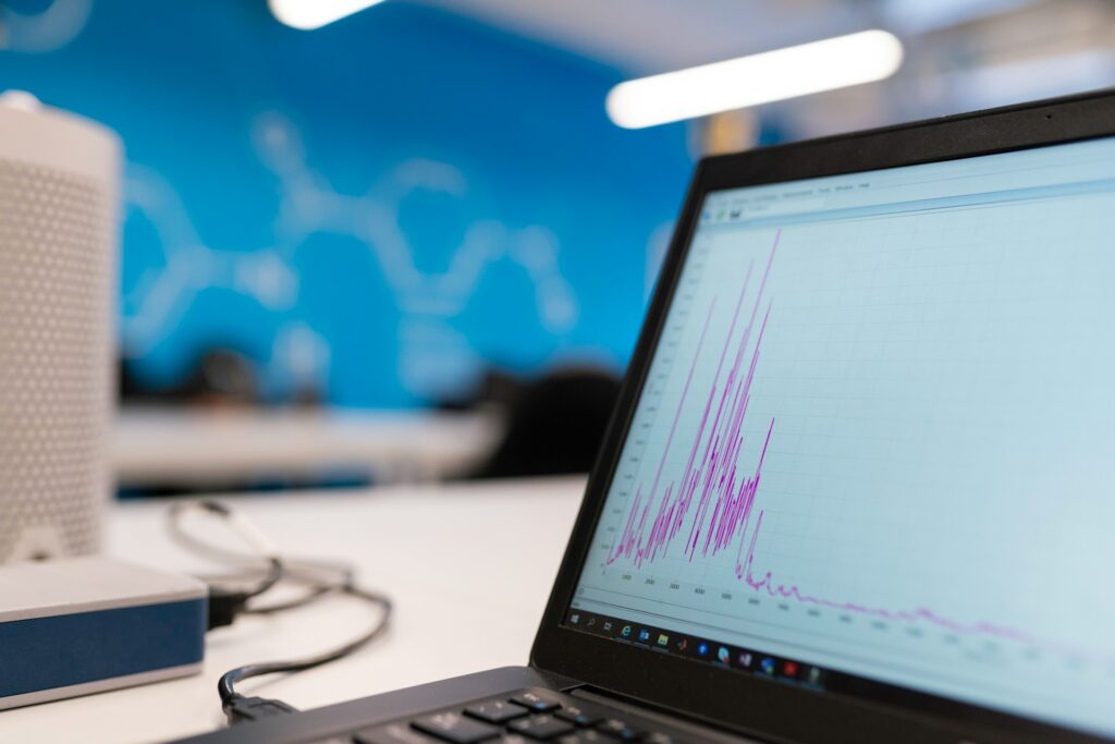 Laptop displaying a purple line graph with fluctuating data peaks on a desk in a modern office with blue wall.