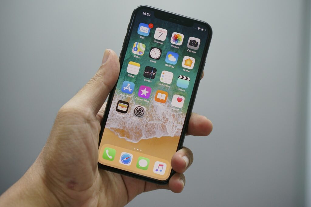 Hand holding a smartphone displaying a home screen with app icons and a beach wallpaper.