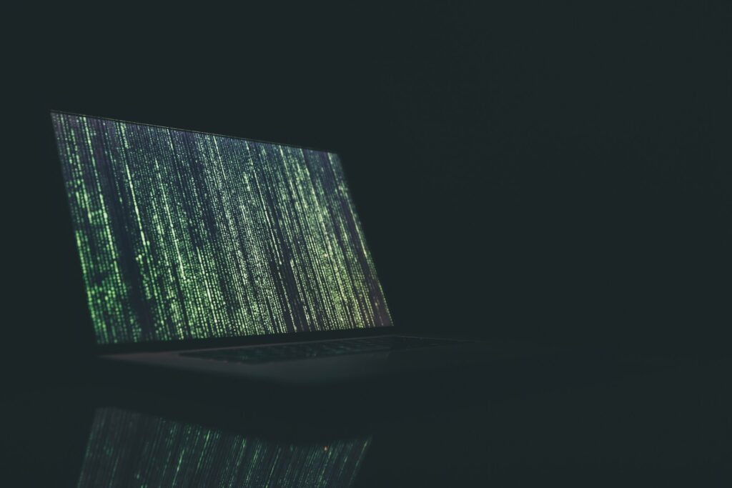 Laptop screen displaying cascading green and white code against a dark background in a dimly lit environment.