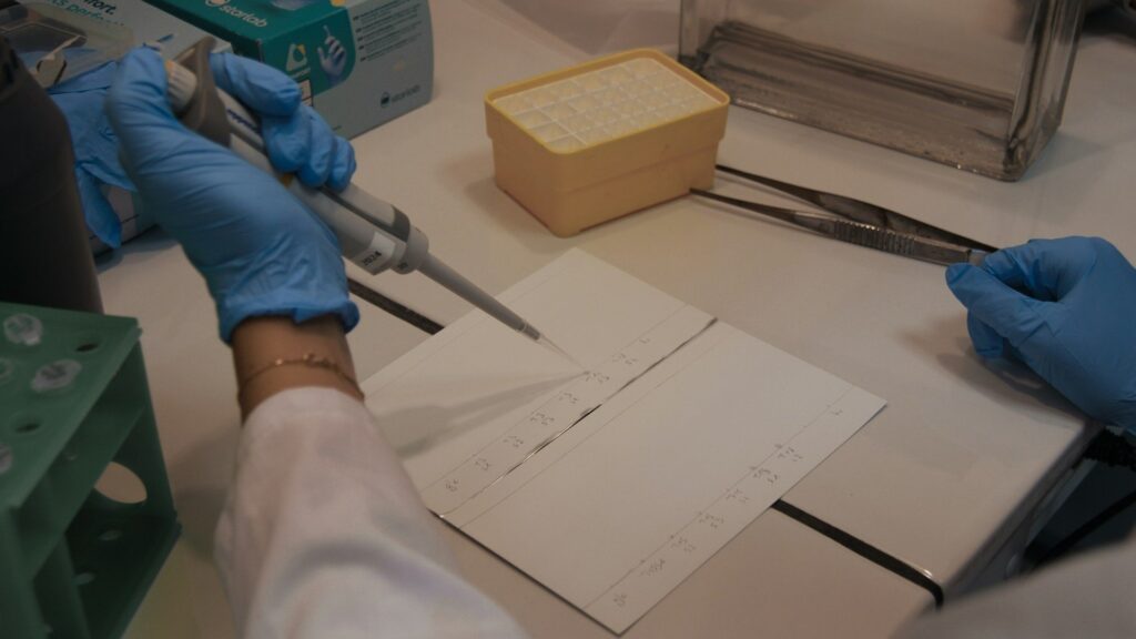 A researcher in blue gloves pipettes samples onto labeled slides in a laboratory setting.