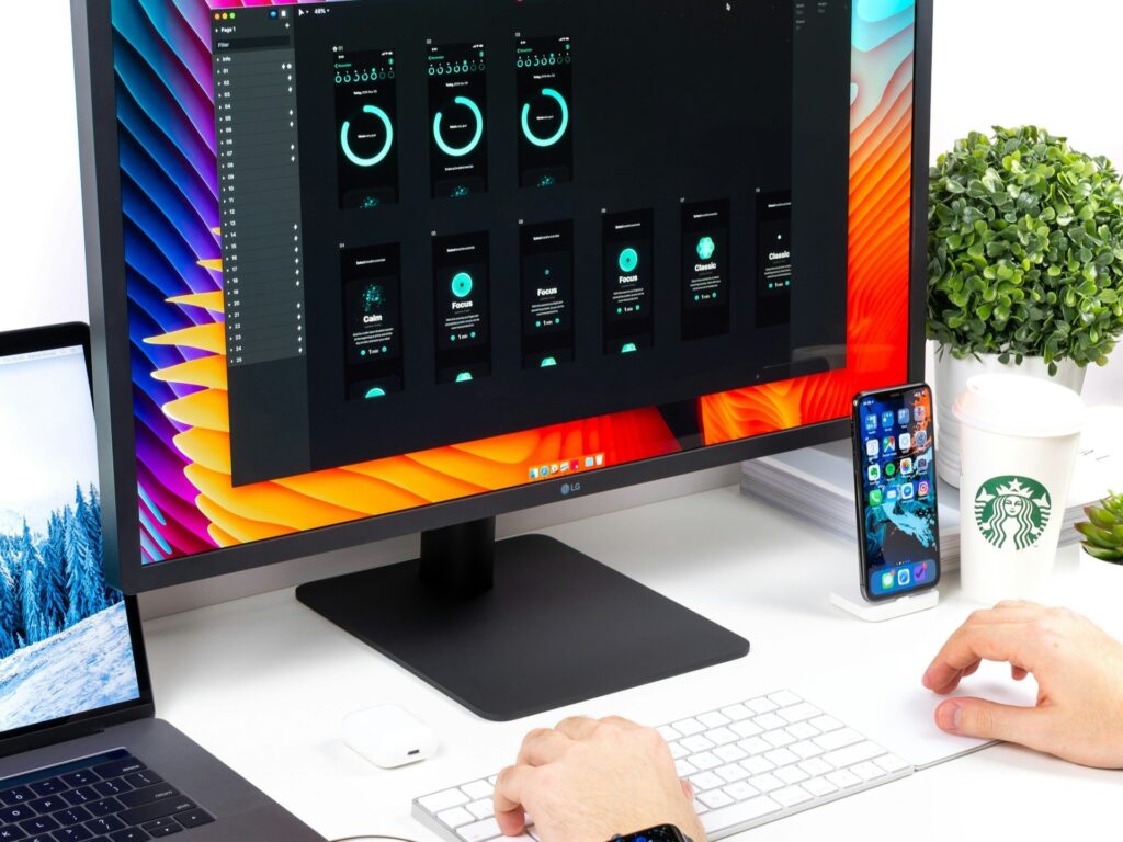 Designer's desk with monitor displaying dark UI interface with cyan circular progress indicators and colorful gradient