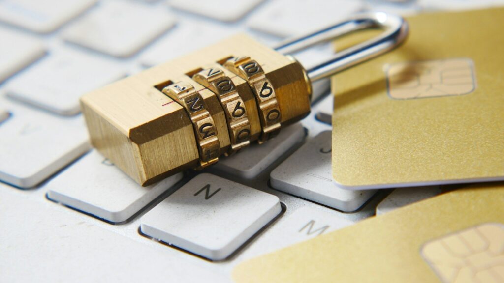 Brass combination padlock resting on computer keyboard keys with a sticky note nearby.