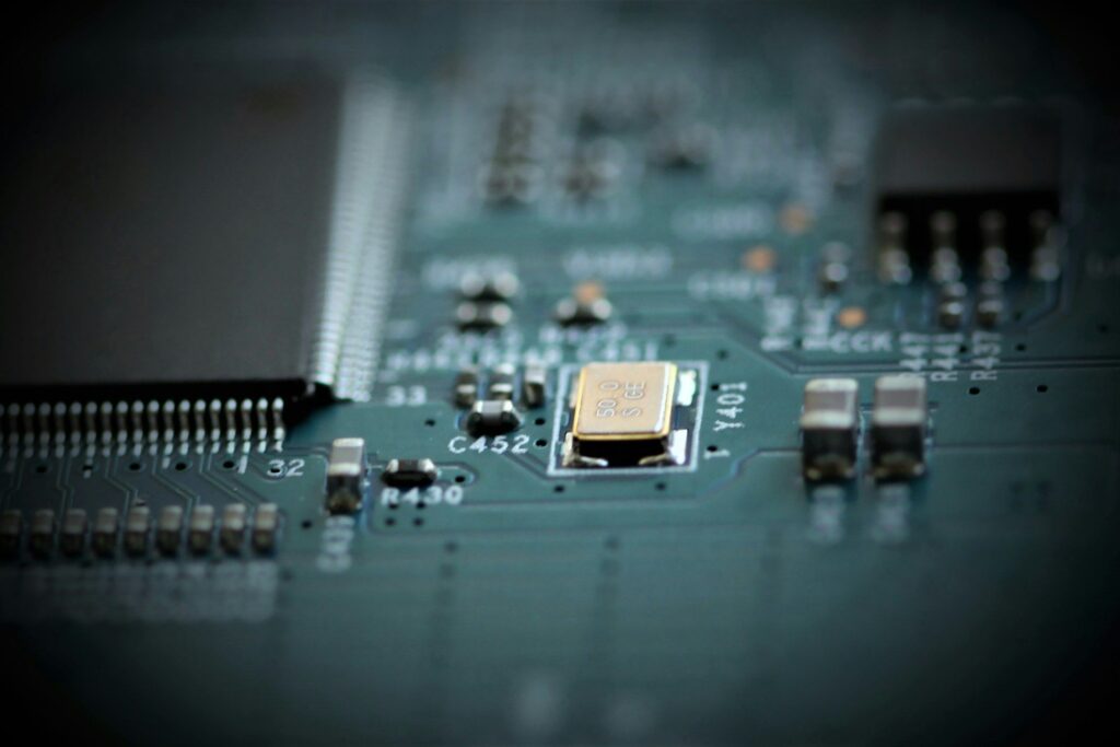 Close-up of a green circuit board with a gold-capped crystal oscillator and various electronic components in sharp focus.