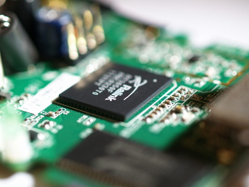 Close-up of a green circuit board with a black processor chip and soldered components in sharp focus.