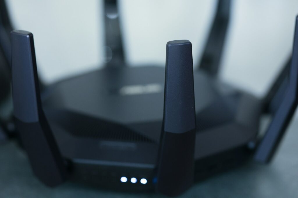 Close-up of a dark wireless router with extended antennas and illuminated status lights on a desk.