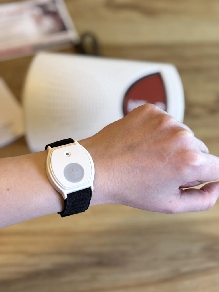 White alert button on a black fabric wristband worn on a wrist above a wooden table